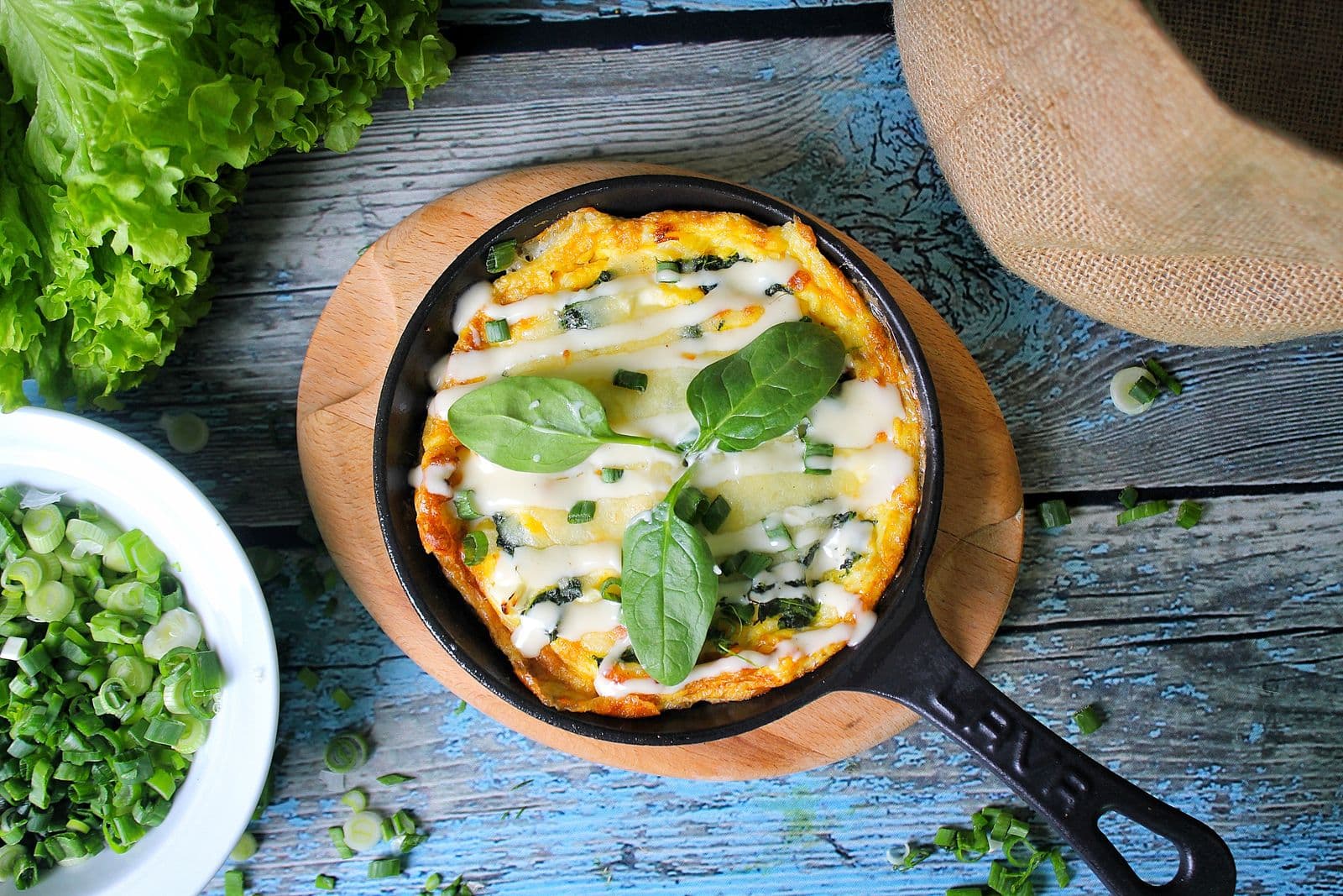 An egg frittata with herbs in a black skillet on a wooden table